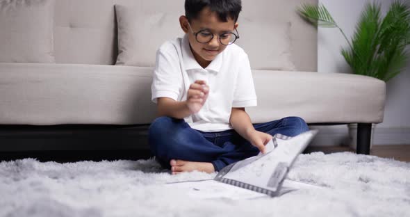 Asian boy wearing glasses sitting and practicing reading on warm floor