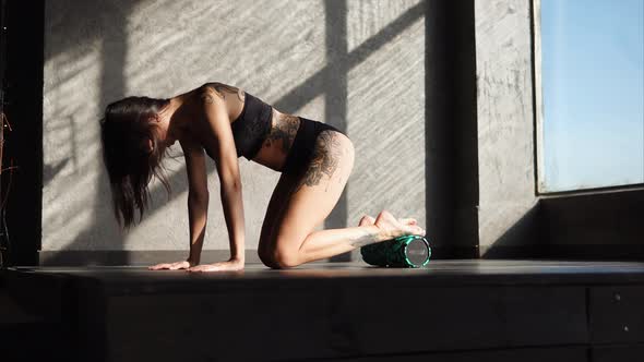 Woman with a Tattoo Uses a Roller for Warming Up Muscles in a Fitness Club