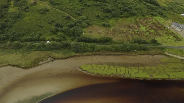 Aerial of small white car traveling along road next to a river in Ireland