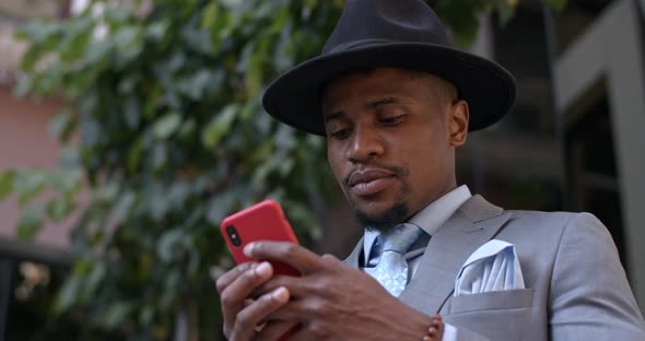 Close Up View of Serious Bussinessman in Hat and Suit Typing Message and Looking at Phone Screen