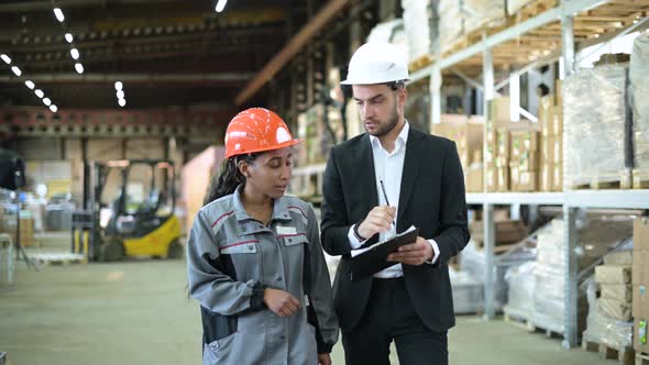 A young manager and a warehouse worker walk through the production workshop