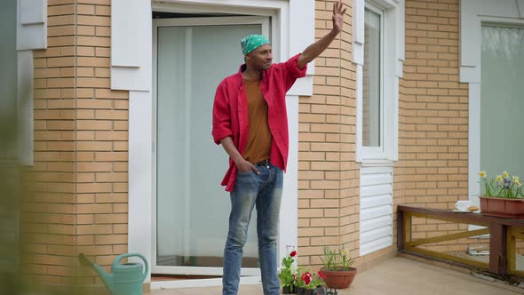 Smiling Young African American Man Standing on Porch Waving to Neighbors