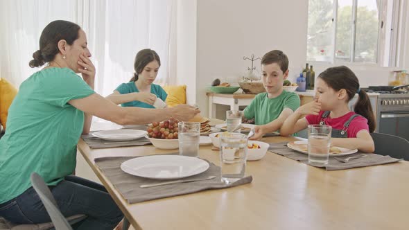 Mother and three kids eating breakfast of pancakes and fruits