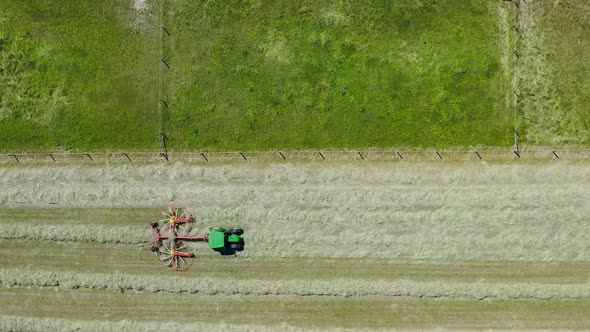 Following a tractor at work with its twin rotor rake driving over a green field drawing clear tracks