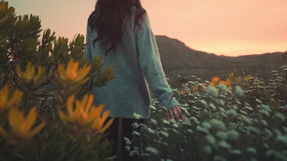 Woman is walking through a field of flowers, touching them gently and moving in slow motion.