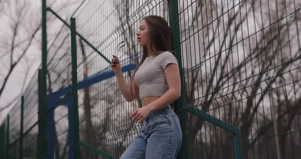 Cute Girl Standing Near Fence on a Stadium in a Park Wearing Eyeglasses