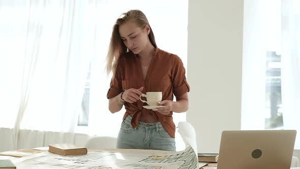 girl in the apartment light works with a design project and drinks coffee