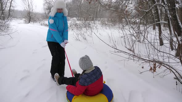Happy Mother Rides a Child on a Sled on a White Snowy Road. Christmas Holidays. A Fun Game for