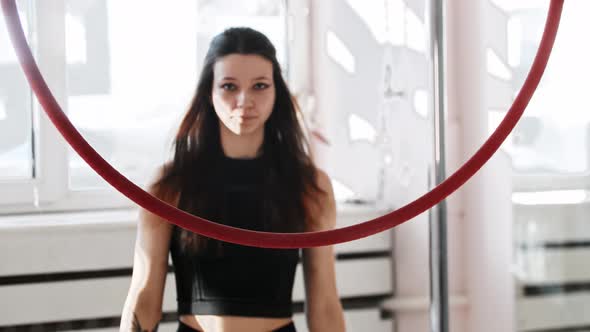 A Young Woman Gymnast Walks to an Acrobatic Ring in the Studio and Looks in the Camera