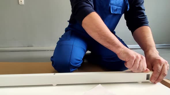 A Man a Handyman in a Blue Jumpsuit is Assembling a Table in Closeup