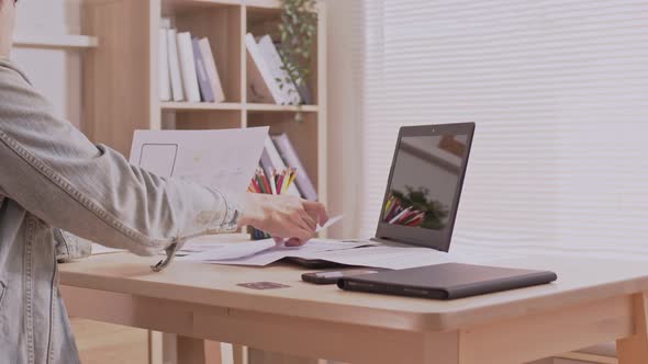 At home, an Asian designer man works on a desk with a laptop, searching for jobs and paperwork.