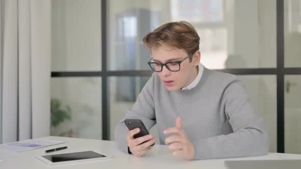 Sad Young Man Reacting to Loss on Smartphone in Office