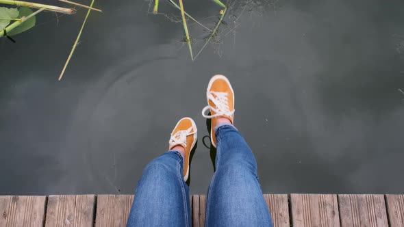 POV Shot Young Woman Sitting on the Pier By the Lake. Just Legs