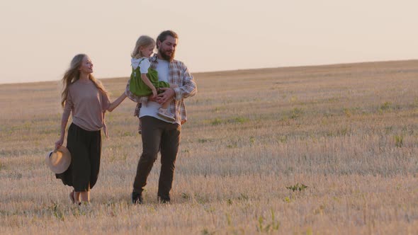 Caucasian Family Farmers Parents with Small Daughter Walking Along Wheat Field in Rural Landscape