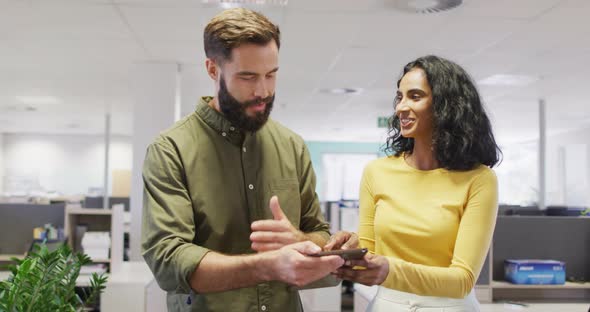 Video of happy diverse businesswoman and businessman using tablet and talking in office