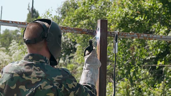 Man Welds Fence Carcass at Trees Slow Motion Backside View