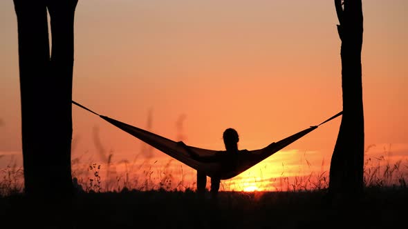 People on vacation. A girl's silhouette in a hammock between trees.