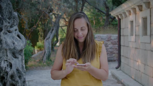 Pretty Woman in a yellow t-shirt reads a message on the phone against the background of nature