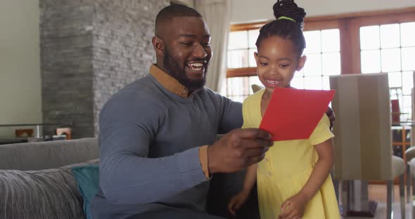 Happy african american daughter giving present to surprised father