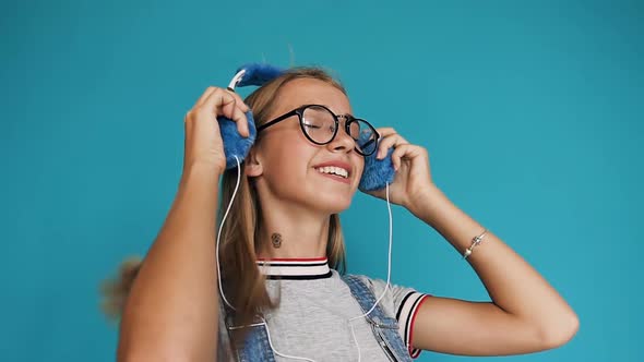 Teenage Girl with Long Hair in Glasses Putting on the Headphones Listening to Music