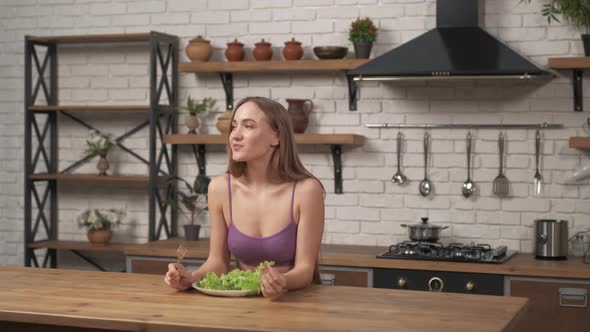 Woman siting at a table on the home kitchen. Sporty girl eating cabbage leaves adheres to a diet