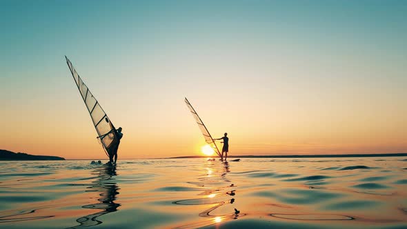 Two Men Are Windsurfing in a Lake at Sundown