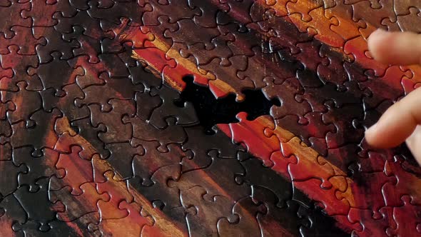 A person's hand finishing a colorful puzzle's last few pieces.