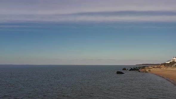 a low angle view over the calm waters by an empty beach, on a day with blue skies. The camera hovers