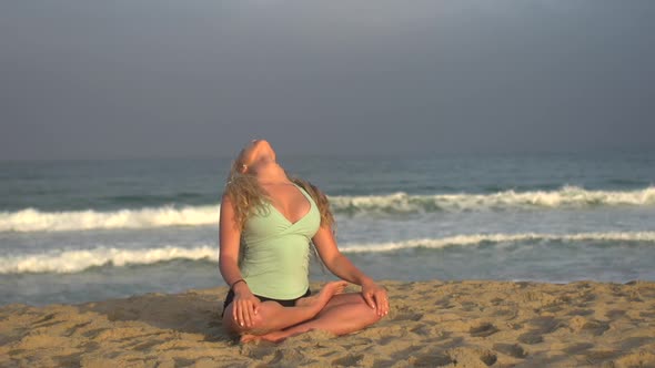 A young woman doing yoga on the beach while sitting.
