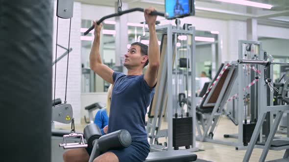 Side view of a woman trainer at a gym who helps a young man to exercise