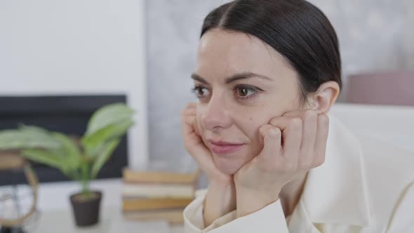 Closeup of Dreamy Caucasian Young Woman Sitting at Workplace Thinking and Smiling