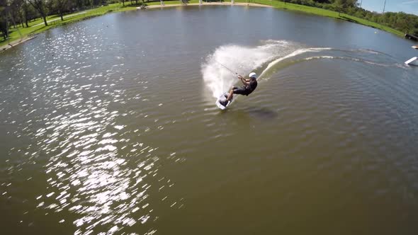 Aerial drone shot of a man riding his wakeboard at a cable park.
