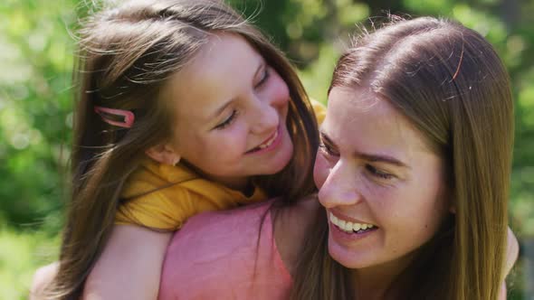 Portrait of caucasian mother carrying daughter on her back in the garden