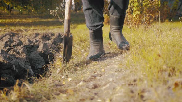 Farmer Goes with Rubber Boots Along Plowed Field. Rubber Boots for Work Use. A Worker Go Down a Heap