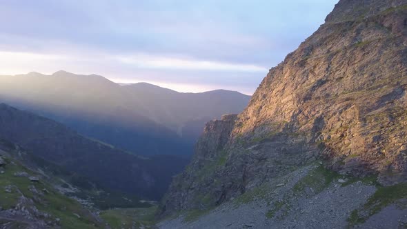 Golden sunlight on cliff face high in mountains of Romania. Aerial view from drone at sunset looking