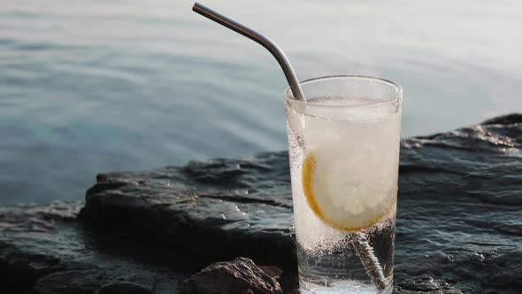 Round Slice of Lemon Falls Into a Glass of Soda Soda Water on Rocky Shore