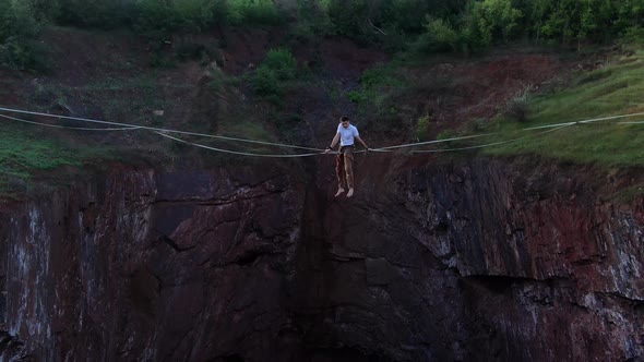 A Man Is Sitting on a Slackline Over a Natural Pit Aerial View Nature