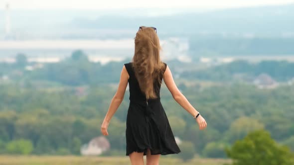 Back View of a Young Energetic Woman in Short Summer Dress Dancing Happily on a Hill Top Outdoors