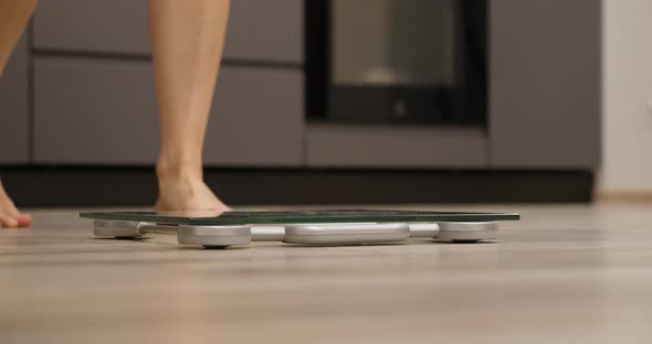 Female feet standing on weighing scales in room.