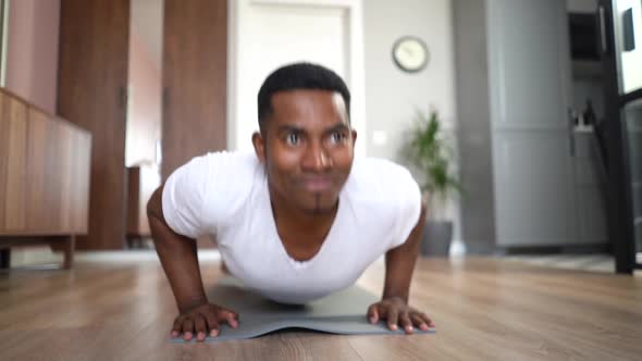 Front View of Cheerful AfricanAmerican Man Doing Pushup on Floor at Living Room Looking at Camera