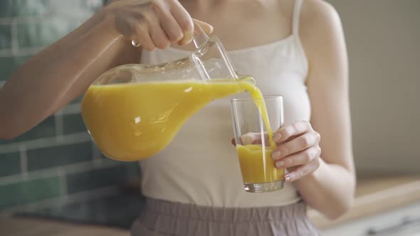 Close Up of Woman Pouring Orange Juice Into the Glass From Jar on Kitchen in Morning