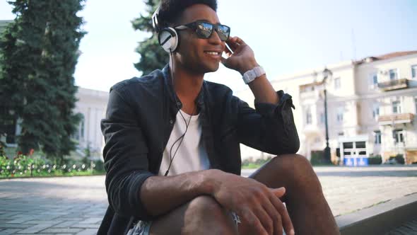 Portrait of Young Stylish Hipster Black Man in White Headphones and Sun Glasses Dancing Outdoor in