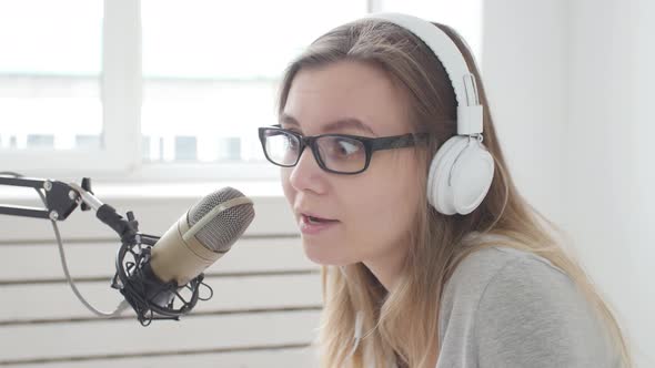 Concept of Streaming and Broadcasting. Young Cheerful Girl in the Studio Speaks Into a Microphone