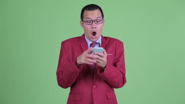 Happy Asian Businessman Using Phone and Looking Surprised