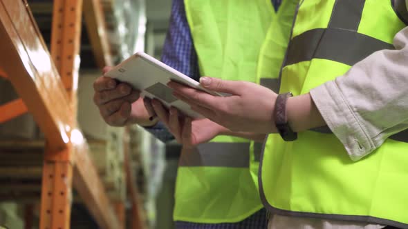 Closeup of the Hands of an Elderly Manager and a Young Employee with a Computer Tablet in a Vest