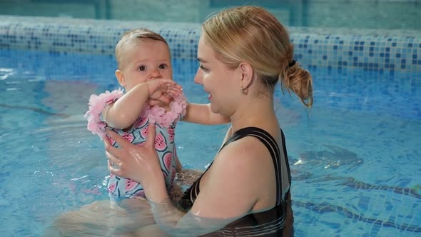 Young Cheerful Mother and Little Daughter Enjoying Swimming in a Swimming Pool