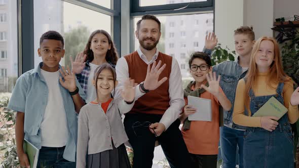 Male Teacher with Middle School Children Looking at Camera and Waving Hands