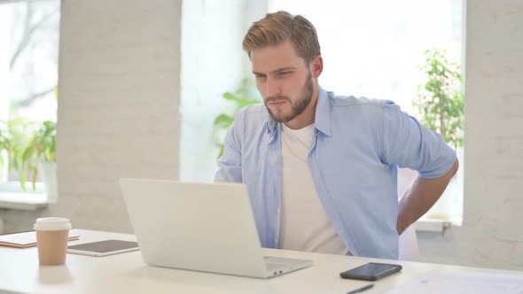 Young Creative Man with Laptop Having Back Pain in Modern Office