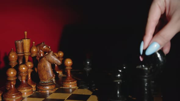 Woman's hand makes a move with the black knight on chessboard.