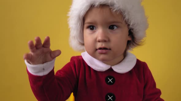 Cute Happy Cheerful Chubby Toddler Baby Girl in Santa Suit Looking On Camera At Yellow Background